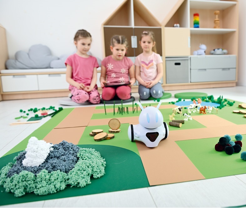 Děti v mateřské škole se baví na koberci s robotem pro kódování a programování, učí se základům technologií a interaktivně rozvíjejí své dovednosti.